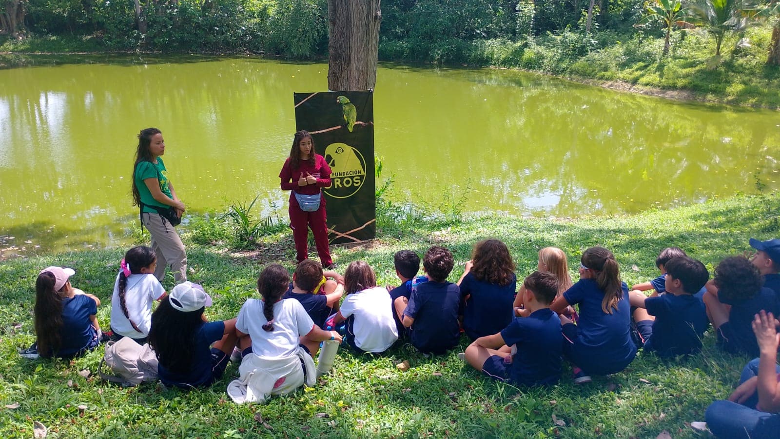 Estudiantes de colegio sentados frente a la laguna del territorio Los Loros escuchando a dos guías de la Fundación antes de una jornada de educación ambiental
